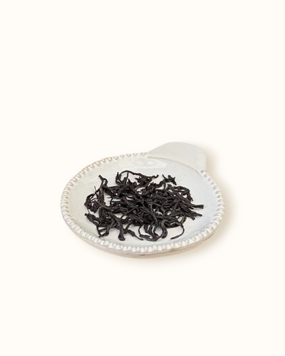 Detailed close-up of dry Lapsang Souchong black tea leaves on a small ceramic dish
