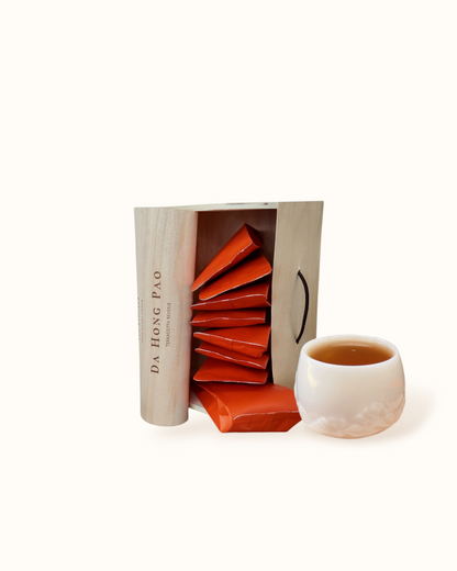 Open Da Hong Pao oolong tea birch wood tea box with orange sachets and amber tea liquor in a white ceramic tea cup
