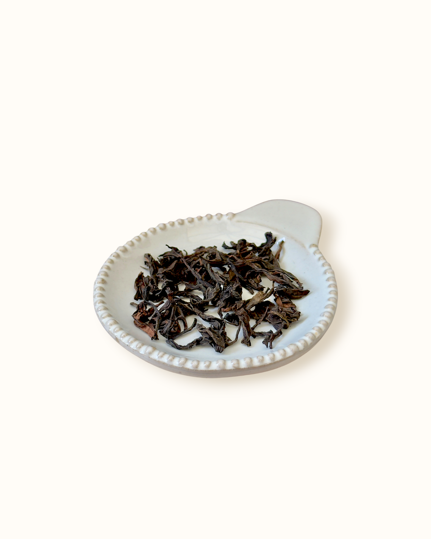 Detailed close-up of dry Da Hong Pao oolong tea leaves on a small ceramic dish