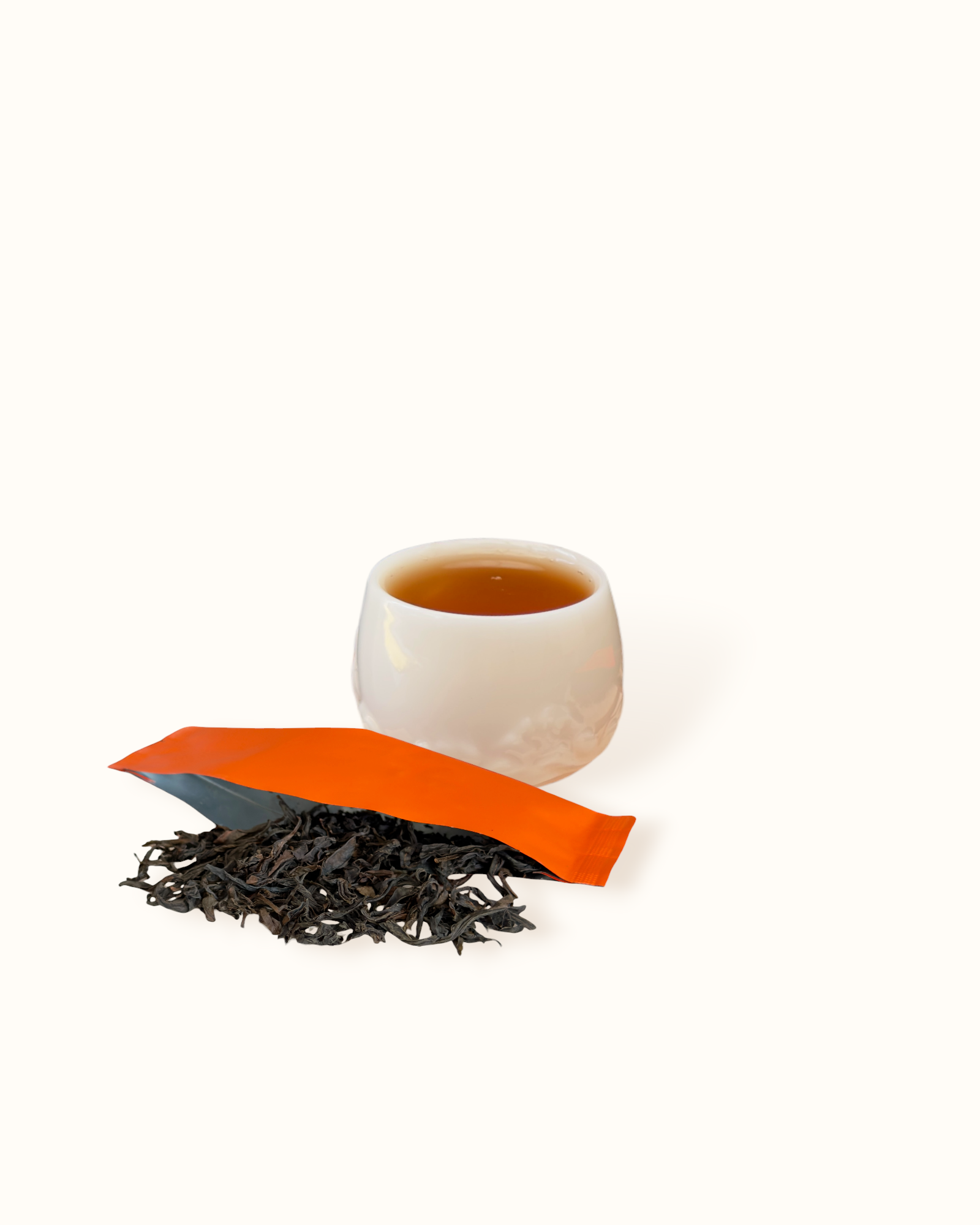Close-up of Da Hong Pao oolong tea leaves with an open orange sachet beside amber tea liquor in a white ceramic tea cup
